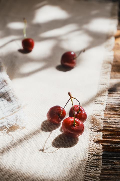 Red cherries resting on textured cream fabric in dappled sunlight