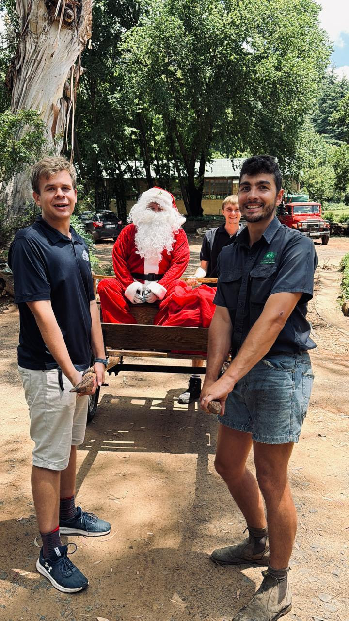 Father Christmas seated in a wooden cart with three helpers outdoors at Wyndford