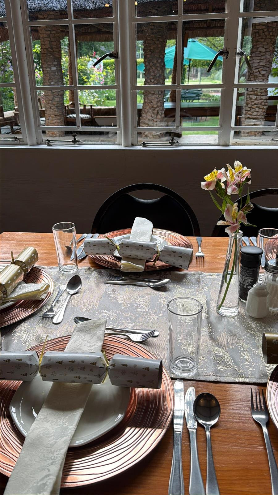 Christmas table set with crackers, copper-coloured plates and flowers beside a window overlooking Wyndford’s garden