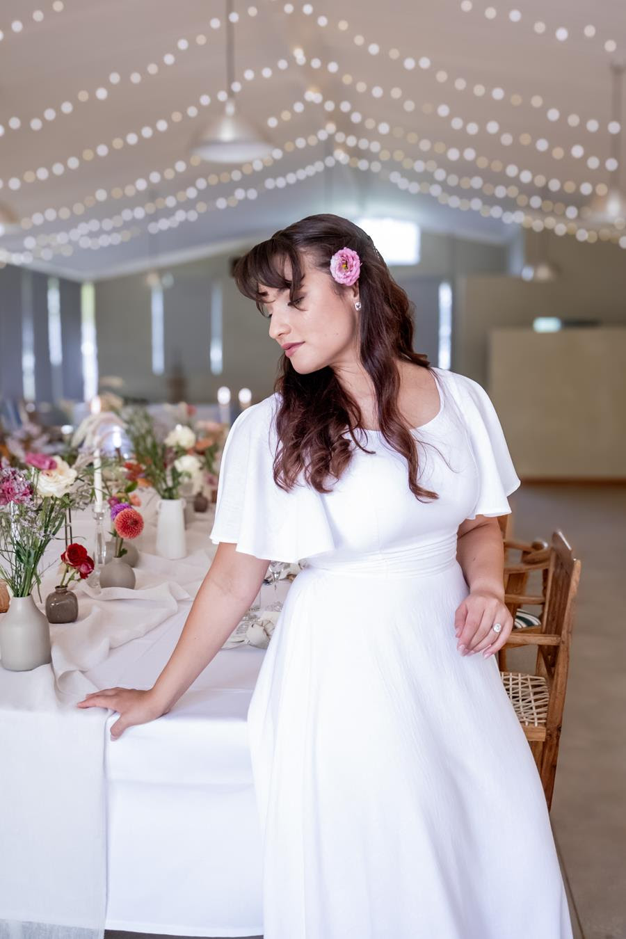 A bride beside a flower-filled reception table beneath strings of fairy lights