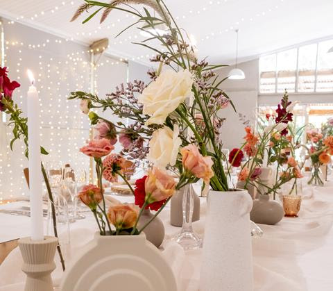 White and pink flowers in ceramic vases, with candles and glassware on a wedding table
