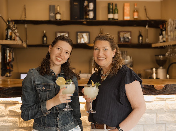 Two guests smiling with drinks at Wyndford’s wooden and stone bar