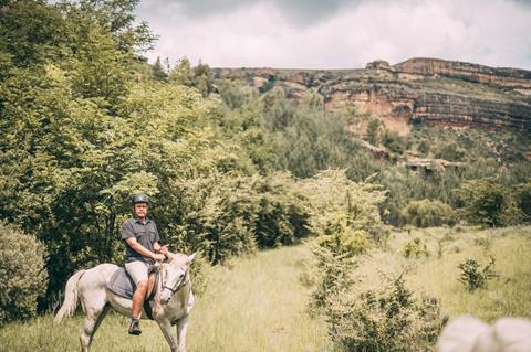 A rider on a grey horse in green countryside beneath sandstone cliffs