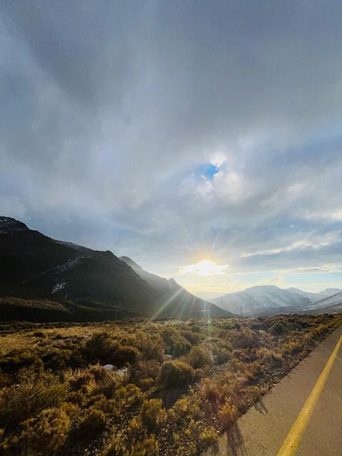 Sunlight breaking through clouds over a mountain valley beside a country road