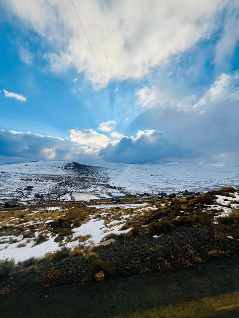 Snow across a mountain landscape beneath blue sky and dramatic clouds